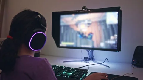 Young girl sitting in front of a computer, playing a game wearing a headset 스톡 동영상 142809241