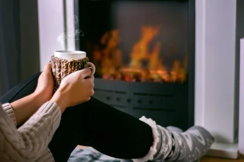 Young girl sitting in front of the fireplace and holding cup of tea in hand Stock Photos