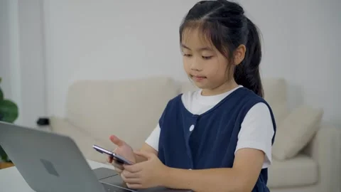 Young girl sitting on sofa using smartphone while laptop open on table in m.. Stock Footage 339377698