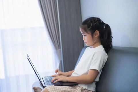 Young girl sitting on sofa using a laptop computer near window with curtain.. Fotos Stock
