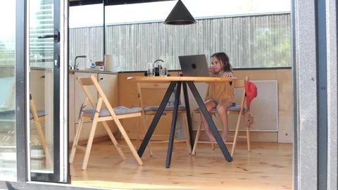 Young girl sitting at a table using a laptop in a tiny house Stock Footage 282522649