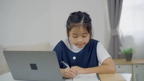Young girl sitting at a table using laptop and writing in notebook focused .. Stock Footage 339377729