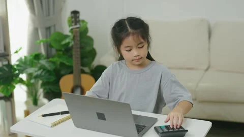Young girl sitting at table working on laptop with book and calculator in a.. Stock Footage 338324252