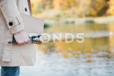 A young girl sketching near a lake in the autumn forest. Stock Photos