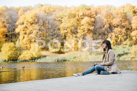 A young girl sketching near a lake in the autumn forest. Stock Photos