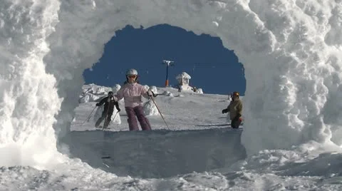 A young girl skier and older male snowboarder ride through snow arch Stock Footage