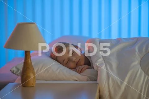The young girl sleeping on the bed. Evening night time Stock Photos