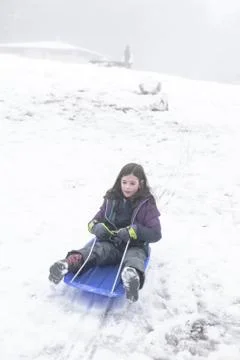 Young girl slides down a hill on a toboggan on a foggy day in the snow Foto stock