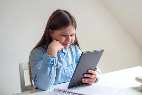 Young girl smiles while using tablet at table Foto stock