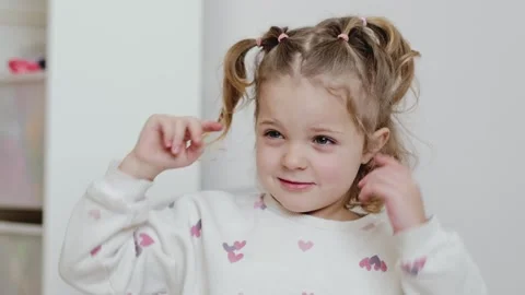 A young girl is smiling and pulling on her pigtails in a bright room filled with Stockbeeldmateriaal 336460338