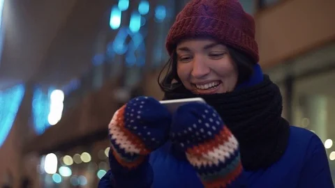 Young girl smiling using smartphone watching video. Knitted mittens on her hands Stock Footage 83070101