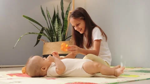 Young girl smiling while entertaining her infant brother with colorful toys Vidéo 287172222