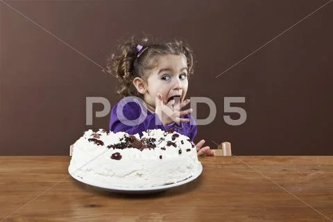 A young girl sneaking a taste of a frosted cake, studio shot Stock Photos