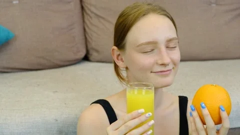 A young girl sniffs orange juice and tries to eat an orange. Stock Footage 200793953