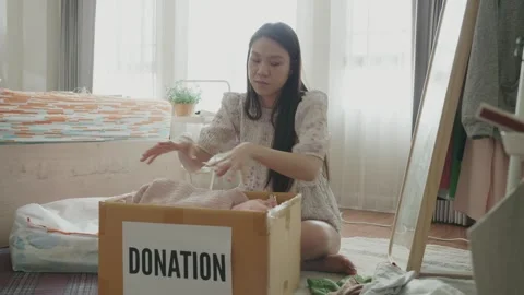 A young girl is sorting through clothes in a donation box Stock Footage 314273465