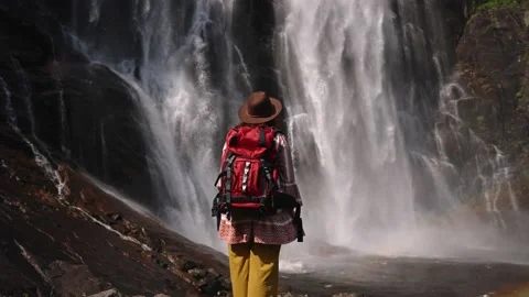 Young girl standing with backpack observing a forest landscape with waterfall Stock Footage 215898345