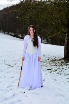 Young girl is standing in long dress in the snow with a bow in hand Stock Photos