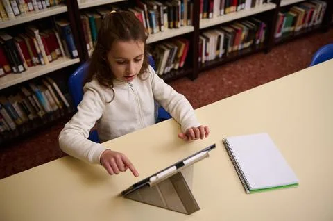 Young Girl Studying in Library Using Tablet With Notebook on Desk Stock Photos
