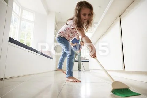 Young girl sweeping kitchen floor, dad in background Stock Photos
