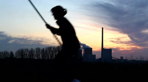 A young girl is swinging with a nice sunset and Power Plant Stock Footage