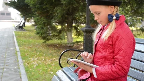 Young Girl with tablet computer sits on bench in autumn in city park. Girl Stock Footage 81263413