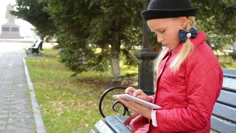 Young Girl with tablet computer sits on bench in autumn in city park. Girl Stock Footage 81325987