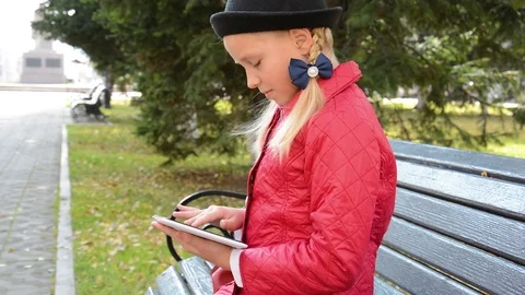 Young Girl with tablet computer sits on bench in autumn in city park. Girl Stock Footage 81326872
