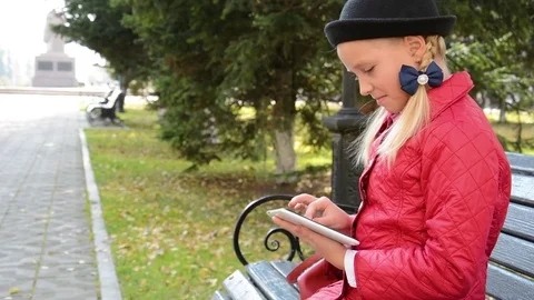 Young Girl with tablet computer sits on bench in autumn in city park. Girl Stock Footage 81327826