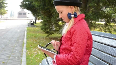 Young Girl with tablet computer sits on bench in autumn in city park. Girl Stock Footage 81328282