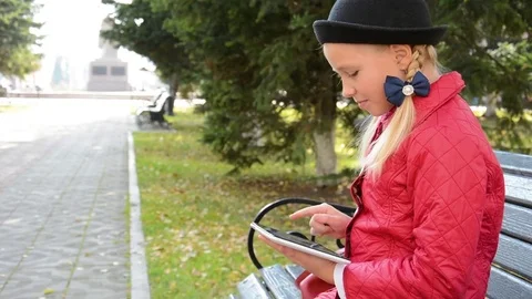 Young Girl with tablet computer sits on bench in autumn in city park. Girl Stock Footage 81329040