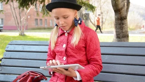 Young Girl with tablet computer sits on bench in autumn in city park. Girl Stock Footage 81329294