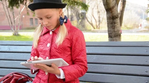 Young Girl with tablet computer sits on bench in autumn in city park. Girl Stock Footage 81329790