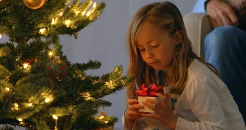 Young girl taking present from beneath Christmas tree. 库存影片 88377014