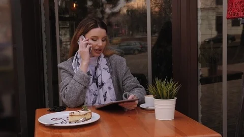 Young girl talking on phone while sitting in coffee shop with tablet computer. Stock Footage 126931148