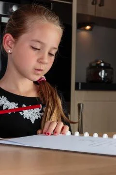 Young girl thinking while doing homework at the kitchen table holding pencil Stock Photos
