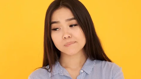 Young girl thoughtfully looking at camera on yellow background biting his lip Stock Footage 125668967