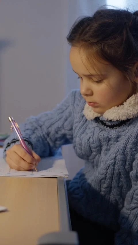 A young girl is thoughtfully studying and writing diligently at a desk in a cozy Video stock 312476341