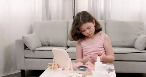 Young girl touching lips while seated at beauty table with makeup products.	 Stock Footage 299313755
