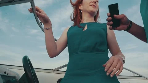 Young girl in turquoise dress in motor boat talk with man hold smartphone. Wind Stock Footage