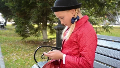 Young girl using app on smartphone sits on bench in autumn in city park Stock Footage 81263499