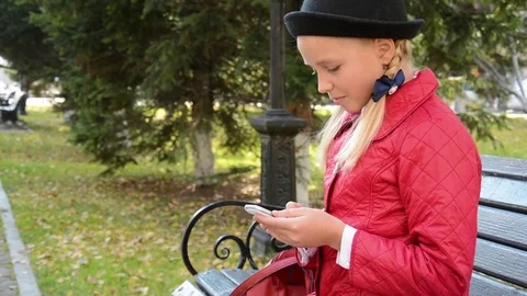 Young girl using app on smartphone sits on bench in autumn in city park Stock Footage 81333623