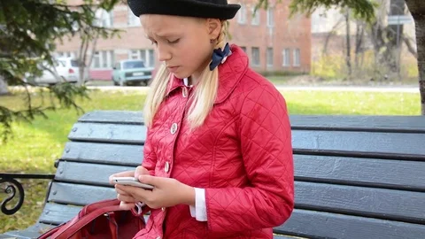 Young girl using app on smartphone sits on bench in autumn in city park Stock Footage 81334018