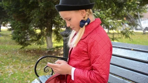 Young girl using app on smartphone sits on bench in autumn in city park Stock Footage 81336305