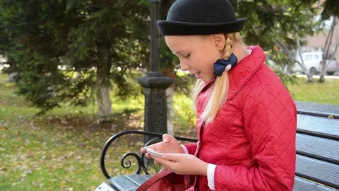 Young girl using app on smartphone sits on bench in autumn in city park Stock Footage 81337867