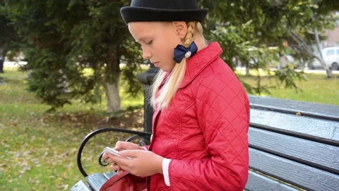Young girl using app on smartphone sits on bench in autumn in city park Stock Footage 81337887