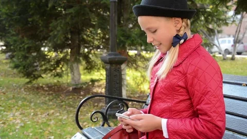 Young girl using app on smartphone sits on bench in autumn in city park Stock Footage 81339638