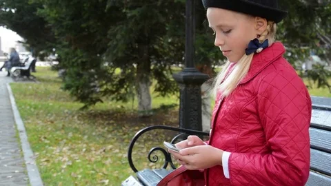 Young girl using app on smartphone sits on bench in autumn in city park Stock Footage 81340035