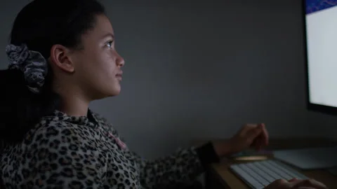 Young girl using a computer and typing as she browses the internet alone at nigh Stock Footage 135604516