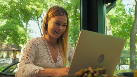 Young girl using her laptop sitting in a restaurant. A girl makes a video ca Stock Footage 202479095