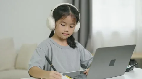 Young girl using laptop computer with headphones at home, taking notes with.. Stock Footage 338323869